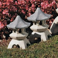 three stone lanterns sitting on top of a lush green field next to pink flowers in the background