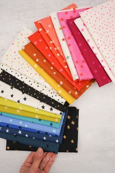 a hand is holding up many different colored stars on the fabric, which are folded in rows