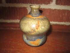 a brown and blue vase sitting on top of a wooden table next to a brick wall