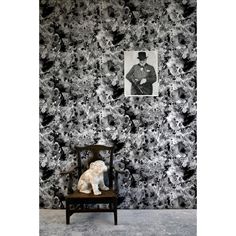 a dog sitting on a chair in front of a wall with black and white flowers