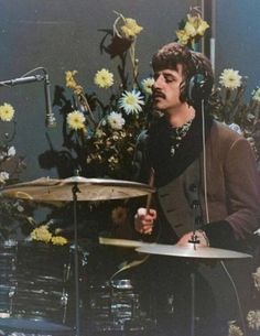 a man with headphones playing drums in front of flowers