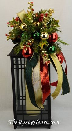 a christmas arrangement in a black lantern with red and green ornaments on it's side