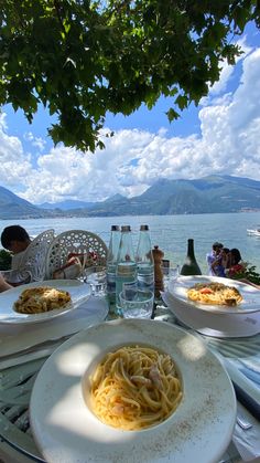 a table that has some plates of food on it with water and mountains in the background