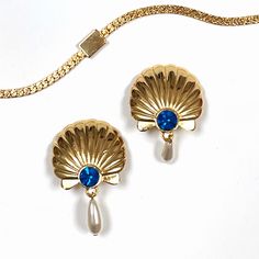 Stunning, opulent pair of vintage clip-ons in gold scallop shell design with a blue Swarovski gemstone and a white drop pearl. They are large, shiny and a little weighty. Perfect for fancy styles and special occasions. Can be matched to several different styles! Made from metal, glass, plastic. Made by West. Each clip on measures 3.5cm wide, 5.5cm long (including the pearl drop) and around 0.5cm thick. Brand new, excellent condition. E Elegant Shell-shaped Earrings, Elegant Shell-shaped Metal Earrings, Elegant Shell-shaped Metal Jewelry, Elegant Shell-shaped Brass Jewelry, Gold Shell-shaped Jewelry For Formal Occasions, Gold Shell-shaped Clip-on Earrings, Coquille Saint Jacques, Scallop Shell, Shell Design