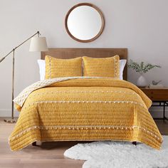 a bed with yellow bedspread and pillows in a white room next to a round mirror