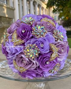 purple and white bridal bouquet with butterfly brooches on glass stand in front of flowers