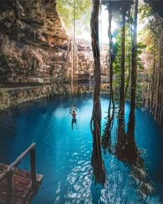 a man standing in the middle of a blue pool surrounded by trees and rocks,