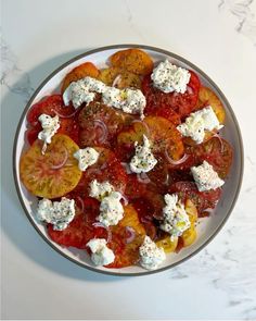 a white plate topped with sliced tomatoes and feta cheese on top of marble counter