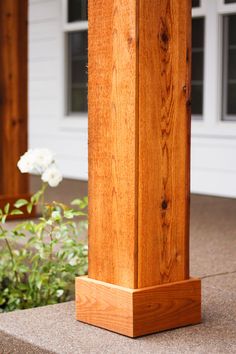 a wooden post sitting on the side of a building next to a flower bed and bushes