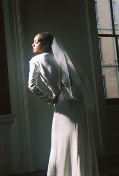 a woman in a white wedding dress and veil looking off into the distance with her hands on her hips