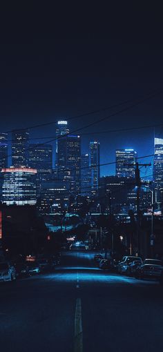 the city skyline is lit up at night, with cars parked on the street below