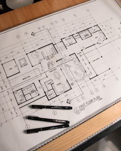 a table that has some pens on it next to a blueprint with a house in the middle