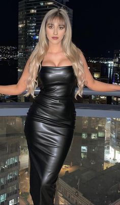 a woman standing on top of a building in a black leather dress with her arms out