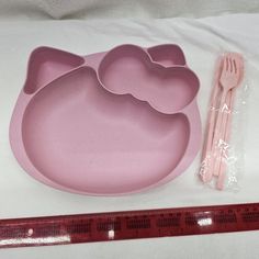 a pink hello kitty shaped plate and fork next to a measuring tape on a white surface