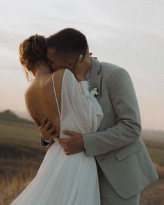 a bride and groom kissing in the middle of a field at sunset with their arms around each other