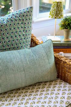 a wicker chair with green and white pillows in front of a basket filled with books