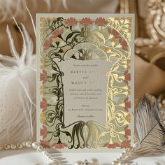 a wedding card with an ornate design on the front and side, surrounded by feathers