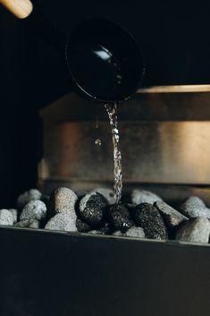 a black pan pouring water onto some rocks