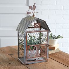 a small metal birdcage sitting on top of a wooden table next to a potted plant