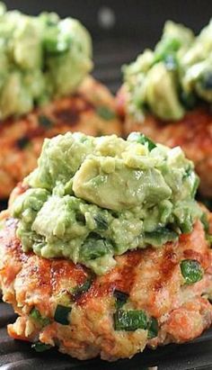 three crab cakes with guacamole on top are sitting on a grill pan