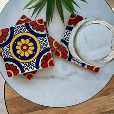 two colorful tiles sitting on top of a table next to a glass jar filled with water