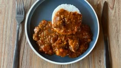 a plate topped with meat and rice on top of a wooden table next to a fork