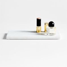 two lipstick bottles sitting on top of a white counter next to a black and gold container