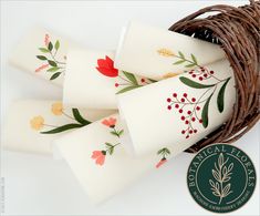 three white cups with red and yellow flowers on them next to a brown wicker basket