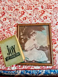 an old book sitting on top of a bed next to a framed photo and a painting