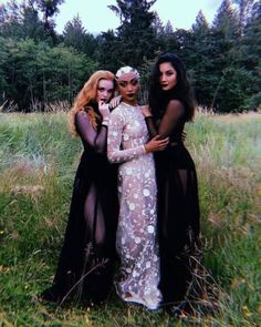 three women in black and white gowns posing for a photo with trees in the background