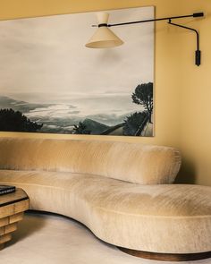 a curved couch sitting in front of a painting on the wall next to a table