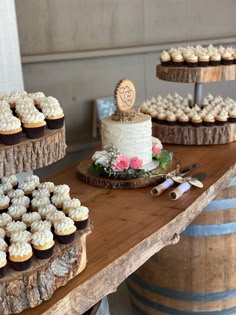 a table topped with lots of cupcakes on top of wooden trays next to wine barrels