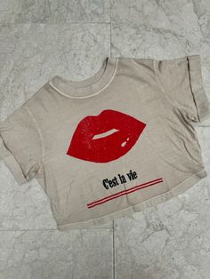 Show off your care free attitude with this Girl Dangerous C'est La Vie Tee with a bold red lips graphic. Perfect for adding a touch of sass to any outfit, this shirt is a must-have for anyone who loves to have fun and live life to the fullest. Color: Sand 100% Cotton Machine wash cold inside out with like colors, tumble dry low Fitted Tan T-shirt With Graphic Print, Cheap Tan T-shirt With Text Print, Pink V-neck Graphic Tee Top, Girl Gang Shirt, Trendy Leopard Print Graphic T-shirt, Bold Red Lips, Swim Shoes, Short Rompers, Board Shorts