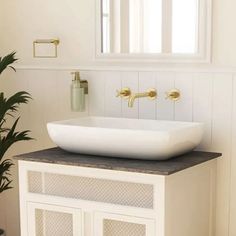 a white sink sitting under a mirror next to a potted green plant in a bathroom