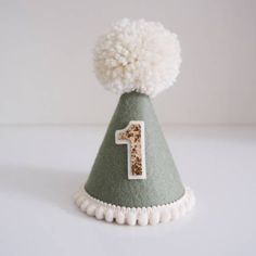 a green and white party hat with a number one on the front, decorated with pom - poms