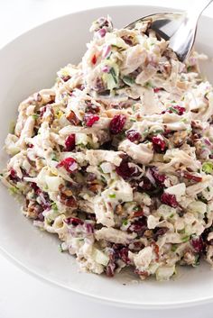 a white bowl filled with chicken salad on top of a table next to a fork