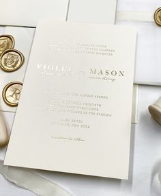 the wedding stationery is laid out on top of white sheets and satin ribbons with gold buttons