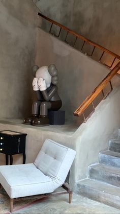 a white chair sitting in front of a stair case next to a table with a lamp on it