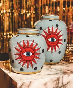 two vases with designs on them sitting on a marble counter top in front of a gold background