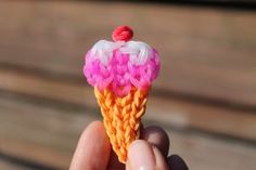 a hand is holding an ice cream cone with pink and orange decorations on the top