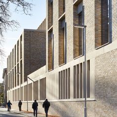 people walking down the sidewalk in front of a brick building with many windows on it