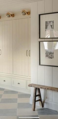 an empty room with white cupboards and wooden bench in the center, along with pictures on the wall