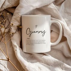 a white coffee mug sitting on top of a bed next to dried flowers and blankets