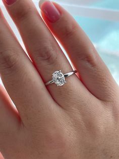 a woman's hand with a diamond ring on top of her finger and the other hand holding an engagement ring