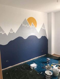 an empty room with mountains painted on the wall and paint supplies in front of it