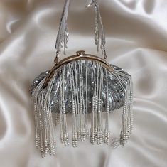 Step into a world of timeless elegance with our exquisite handmade silver evening bag. Crafted with meticulous attention to detail, this enchanting accessory seamlessly blends tradition with modernity. Each delicate beads and sequins has been carefully chosen and skillfully hand-sewn, creating a mesmerizing symphony of shimmering ivory tones that catch the light with every movement. The  bag's intricate sequins and beadwork showcases a stunning fusion of classic design and contemporary flair, making it a perfect match for brides seeking a touch of refined charm. The bag's compact size and comfortable handle make it not just a beautiful piece, but also a functional one, allowing you to carry your essentials effortlessly on your special day. Elevate your bridal ensemble with the timeless all Potli Bag, Handmade Clutch, Potli Bags, Day Bag, Bag Handmade, Hand Sewn, Handmade Silver, Perfect Match, Evening Bags