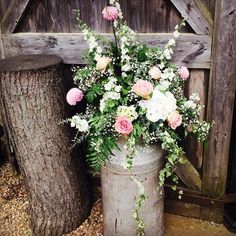 a large metal bucket filled with lots of flowers next to a wooden fence and tree