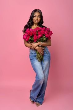 a woman is holding roses in her hands and posing for the camera on a pink background