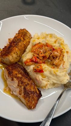 two pieces of meat and mashed potatoes on a white plate with silver utensils