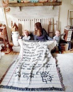 a woman and two children sitting on a bed with a blanket that has writing on it